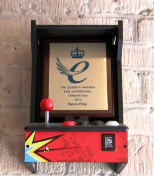The Queen's Award won by Neon Play displayed in an arcade machine frame.
