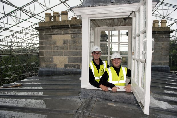 2 men in hard hats on the roof of a historic building.