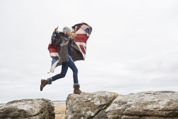 Woman jumping between 2 rocks carrying a Union Flag.