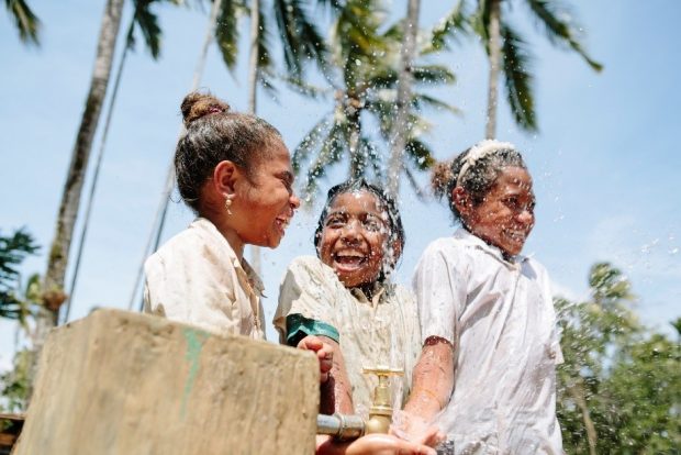 3 girls in Timor Leste playing with water from a tap.